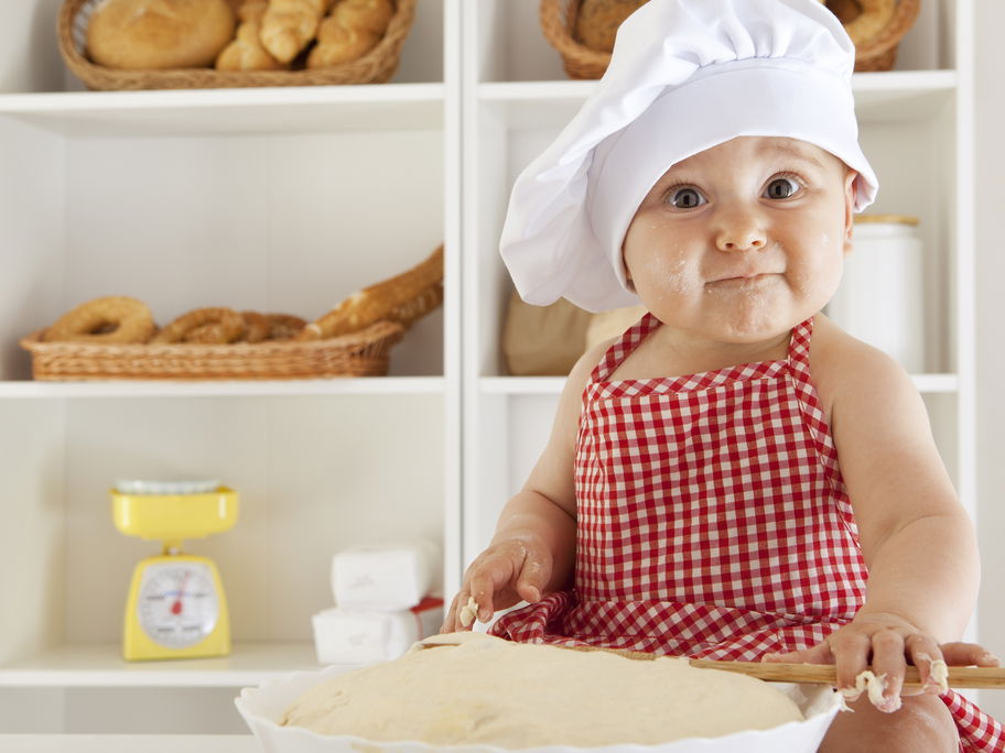 Baby mit Bäckermütze macht Brotteig.