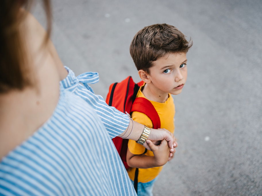 Mutter hält die Hand ihres Sohnes und bringt ihn zur Schule.