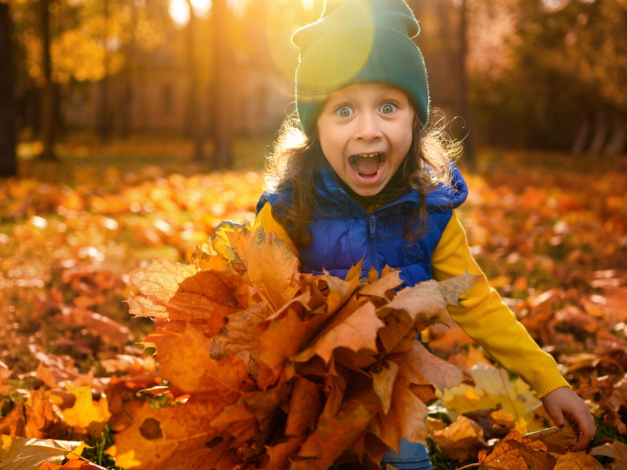 Lachendes Mädchen spielt im Herbstlaub.
