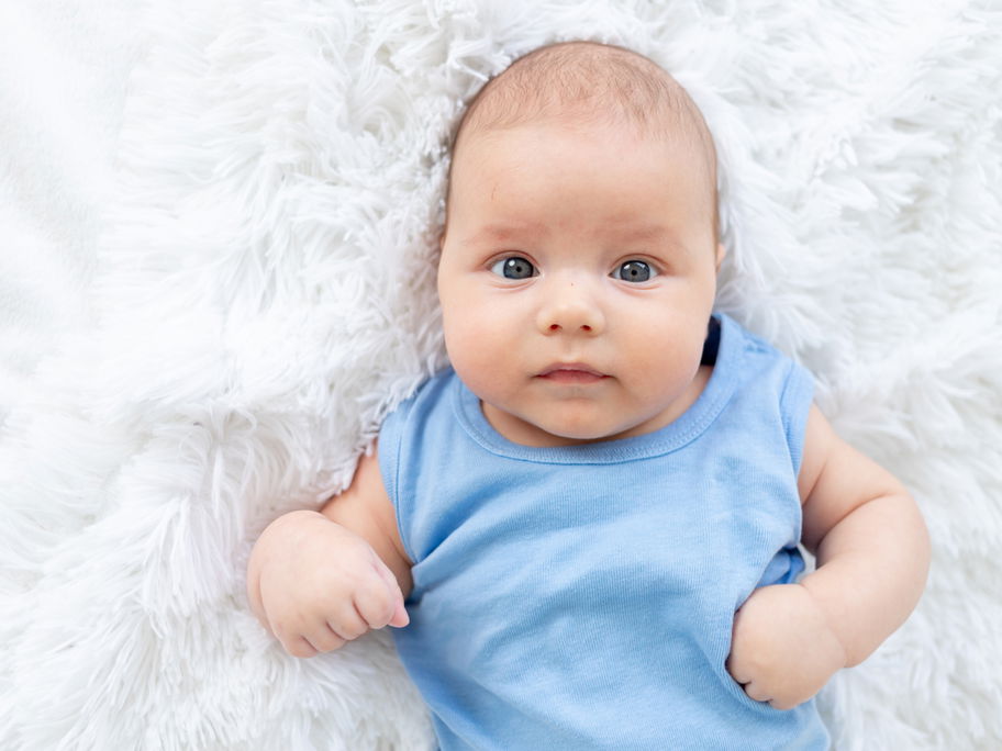 Baby-Junge in einem blauen Body liegt auf einem Lammfell