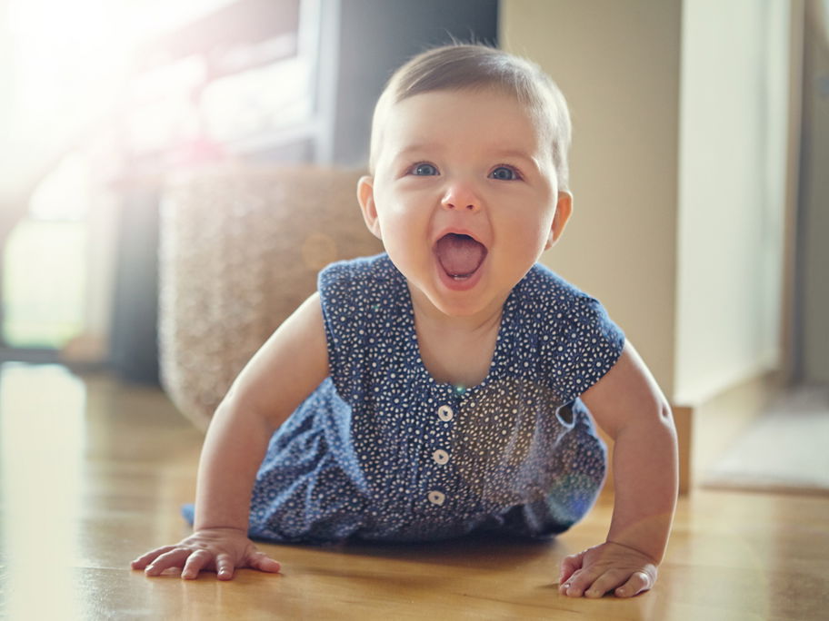 Baby-Mädchen robbt auf dem Boden und lacht mit offenen Mund.