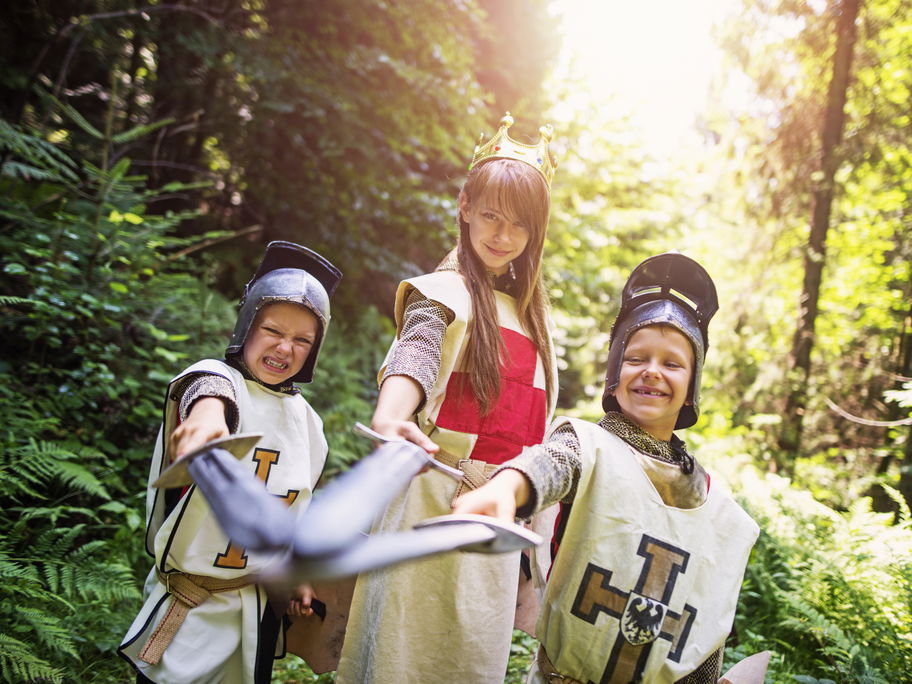 Zwei Jungs und ein Mädchen sind verkleidet als Ritter und Königin im Wald.
