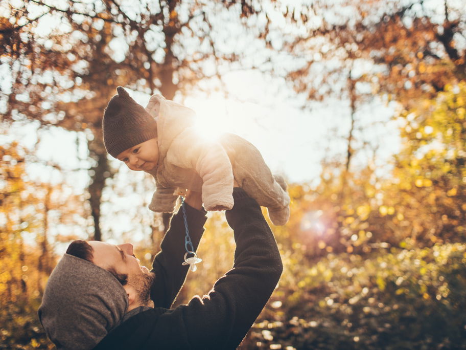 Papa hält Baby hoch im herbstlichen Wald