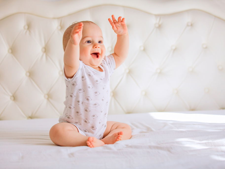 Baby sitzt lachend auf dem Bett.