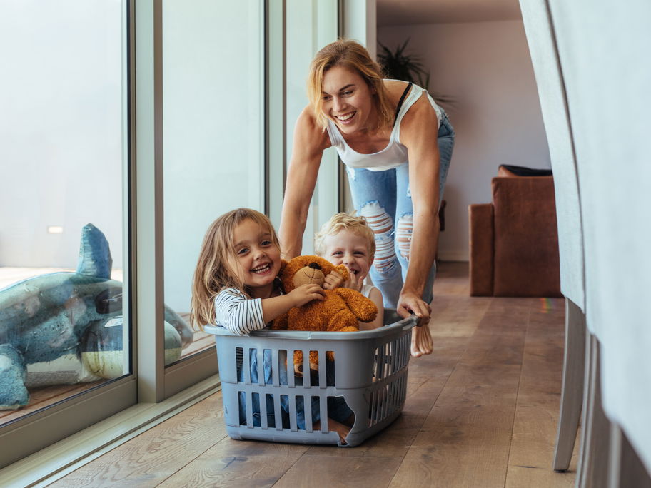 Lachende Mutter schiebt ihre Kinder in einem Wäschekorb.