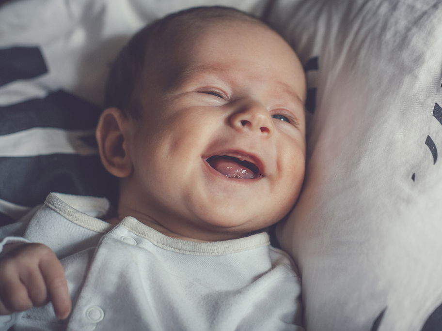 Kleiner Baby-Junge lacht zufrieden und liegt auf dem Bett.
