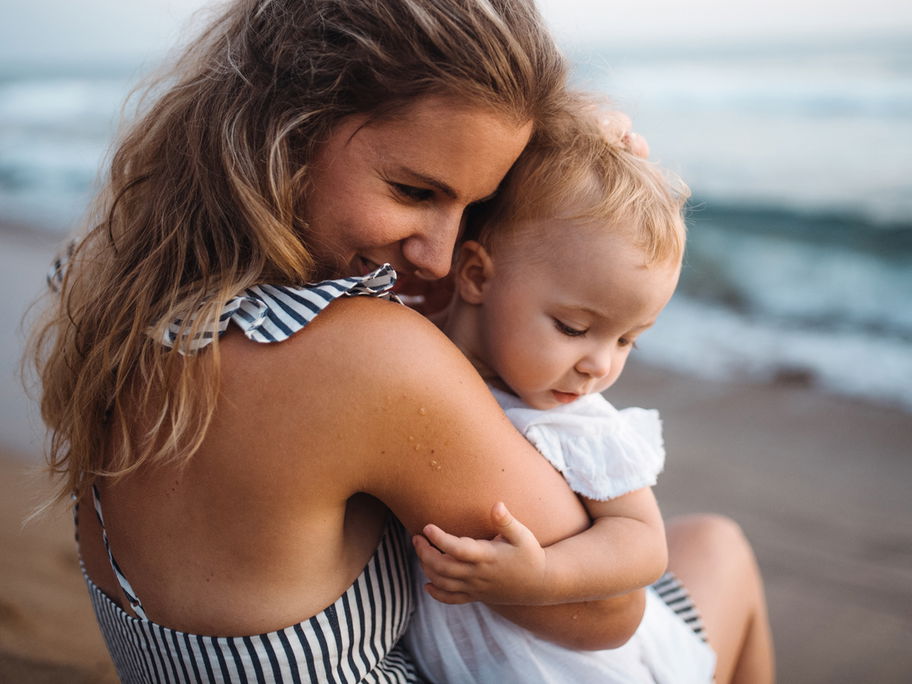 Mama kuschelt mit Baby bei Reise am Strand