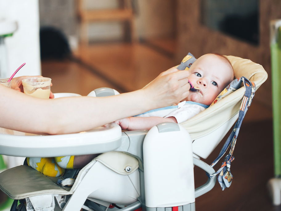 Baby liegt und isst im Hochstuhl