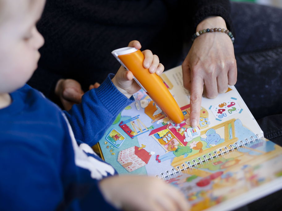 Ein kleiner Junge schaut gemeinsam mit einer Frau ein Tiptoi-Kinderbuch an.