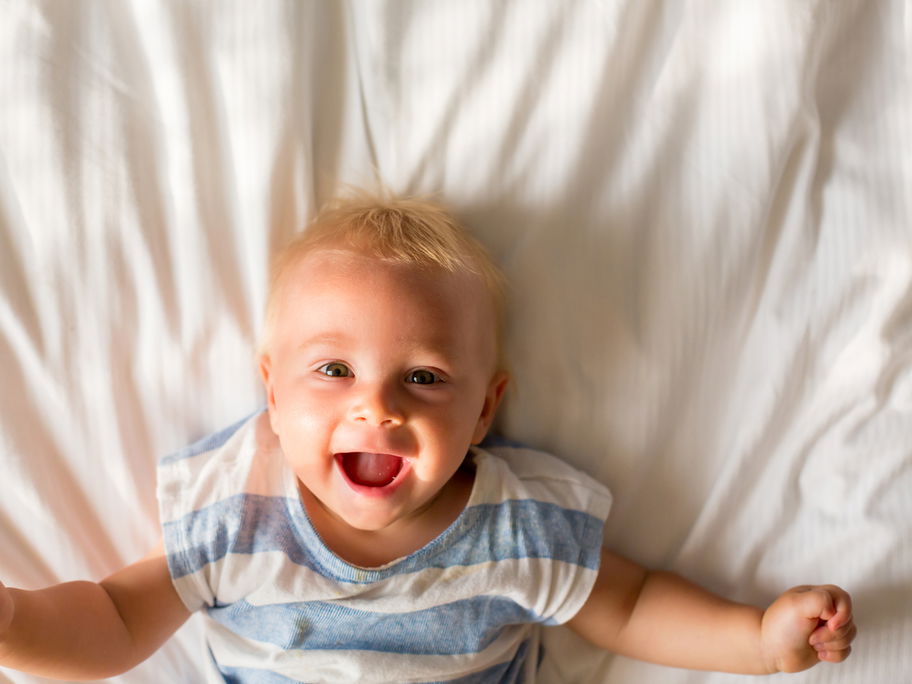 Baby-Junge liegt auf dem Bett und lacht.