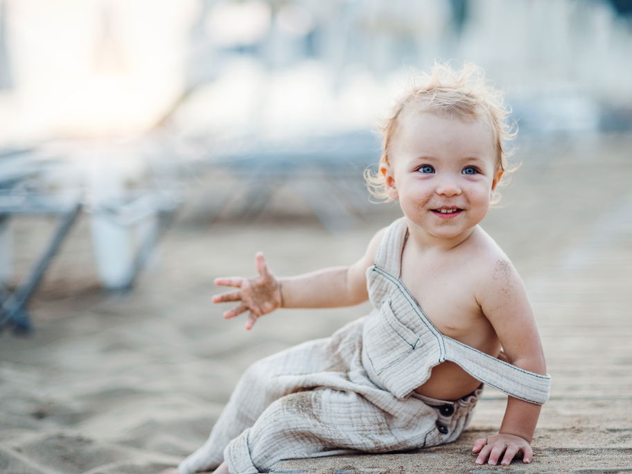 Ein kleines Mädchen sitzt mit Sand an den Händen am Strand.