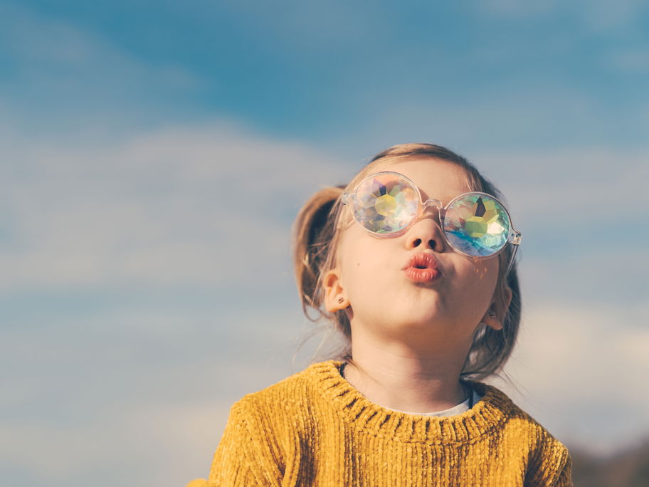 Ein kleines Mädchen schaut mit dicker Sonnenbrille in den Himmel.