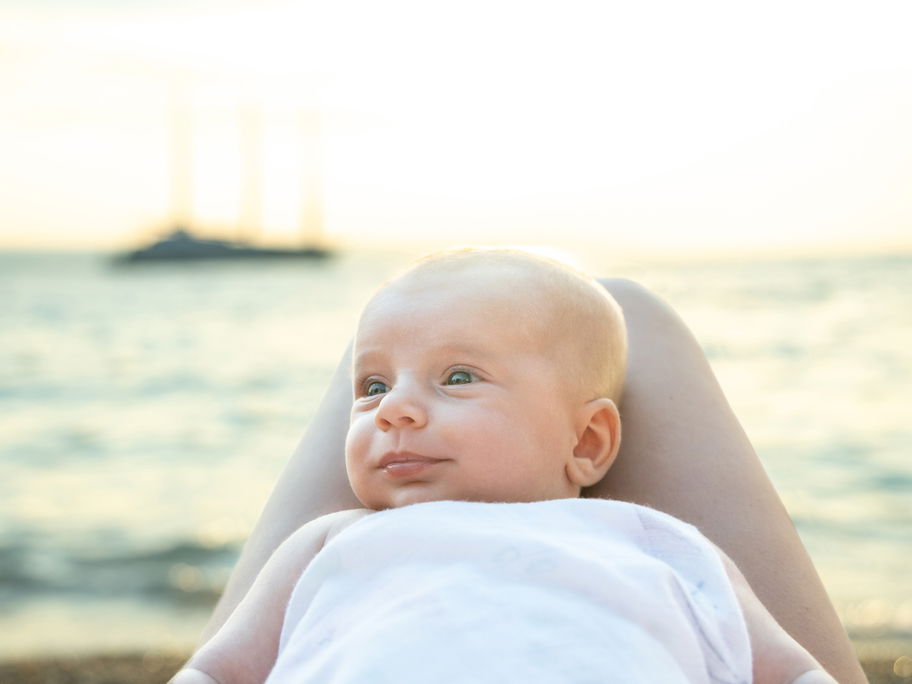 Am Meer: Ein Baby liegt zufrieden auf dem Schoss