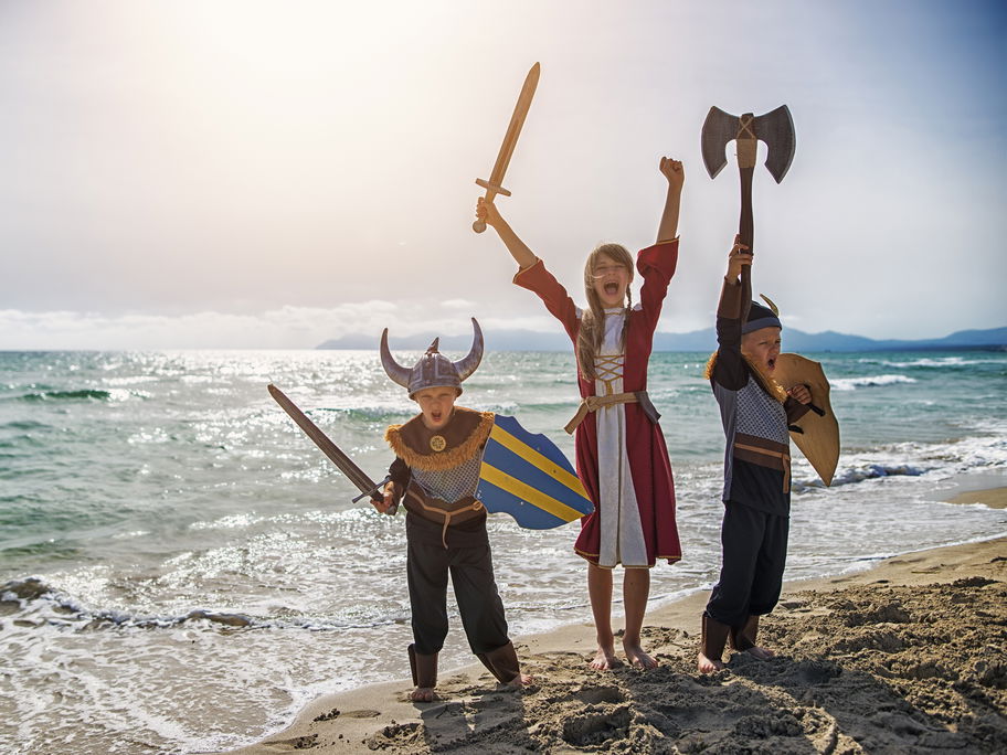 Zwei Jungen und ein Mädchen sind verkleidet als Wikinger am Strand.