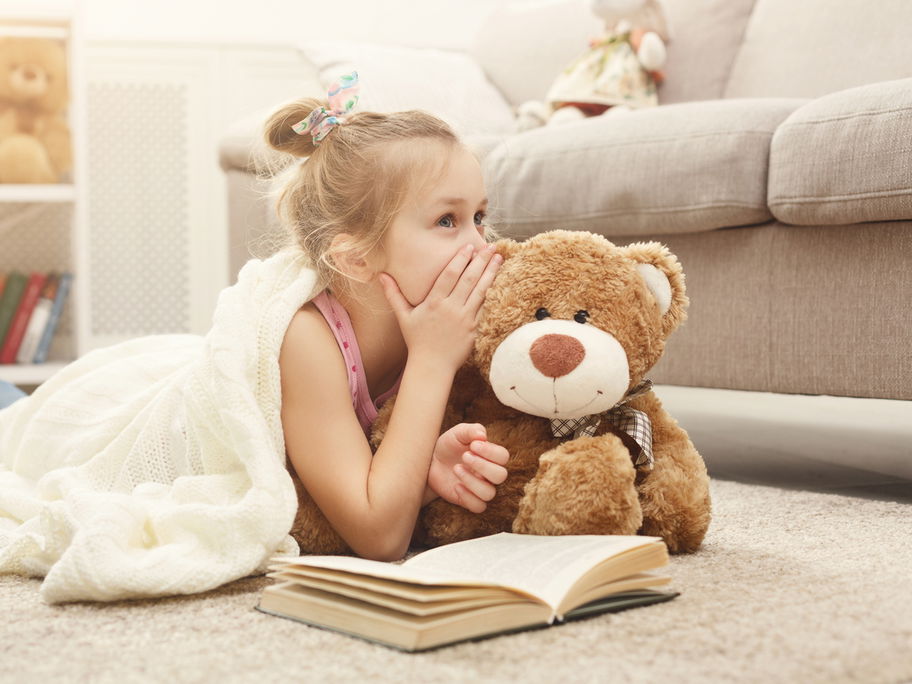 Kleines Mädchen flüstert ihrem Teddy ein Geheimnis ins Ohr.