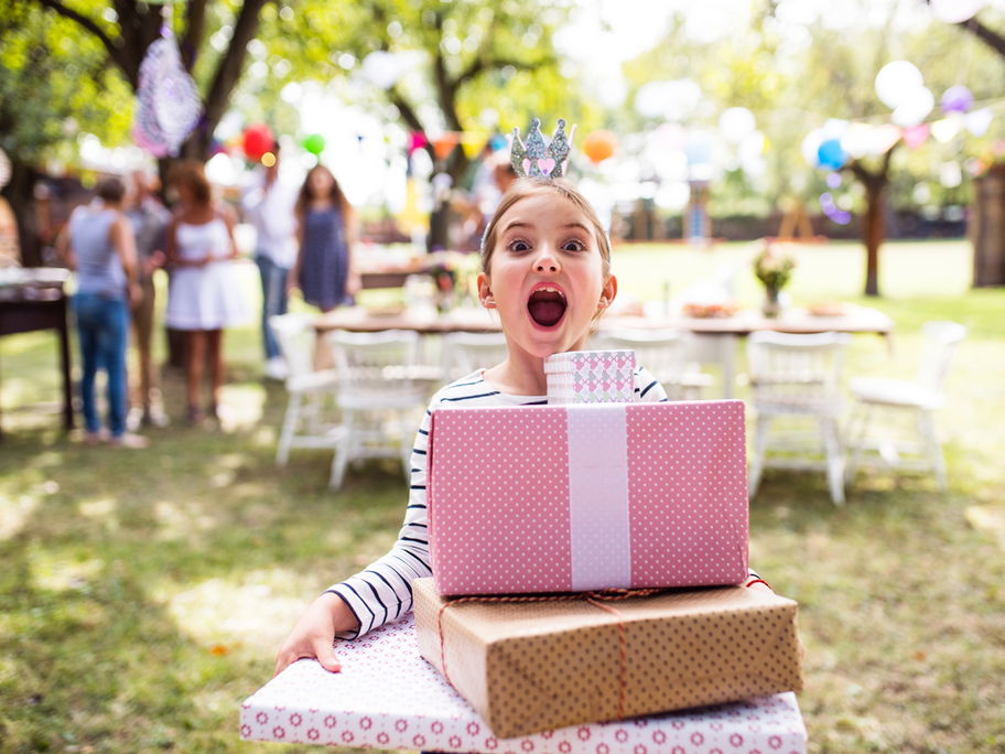 Mädchen feiert Geburtstag und hält viele Geschenke im Arm.