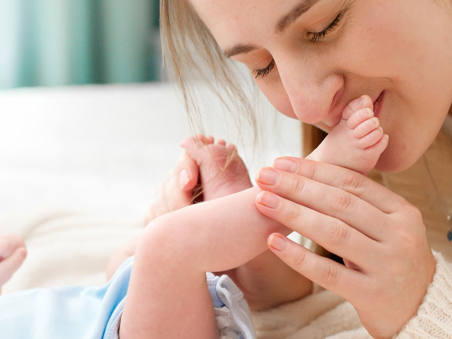 Mama küsst die Füßchen ihres Babys.