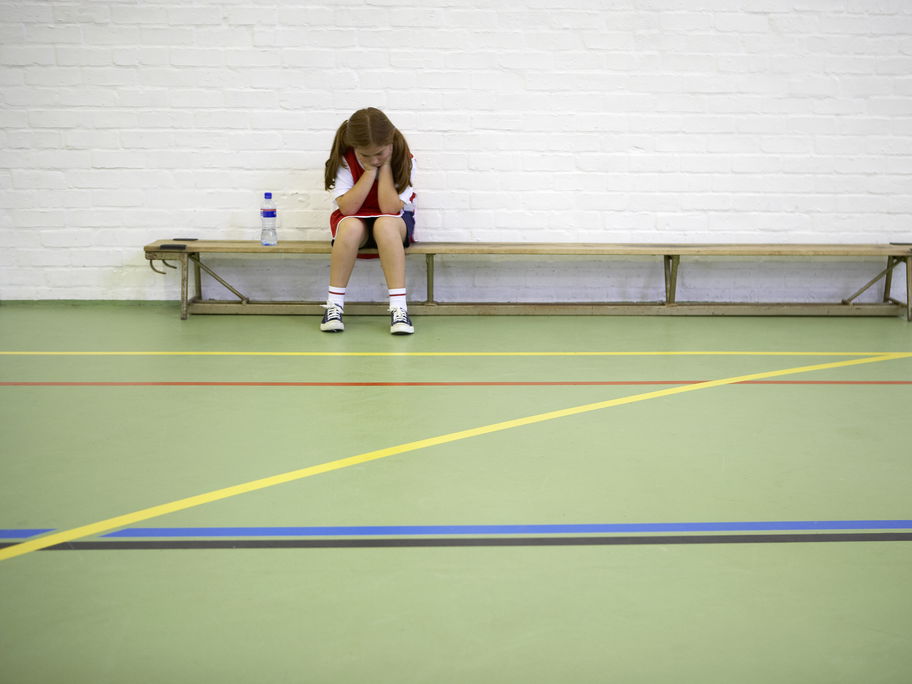 Ein Mädchen sitzt beim Schulsport frustriert auf der Bank.