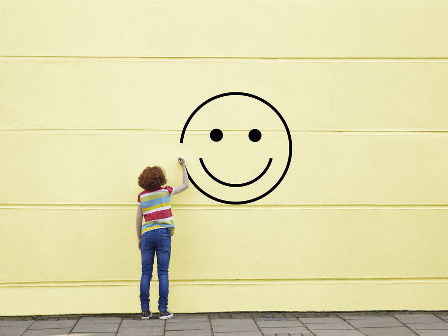 Mädchen malt Smiley an gelbe Wand.