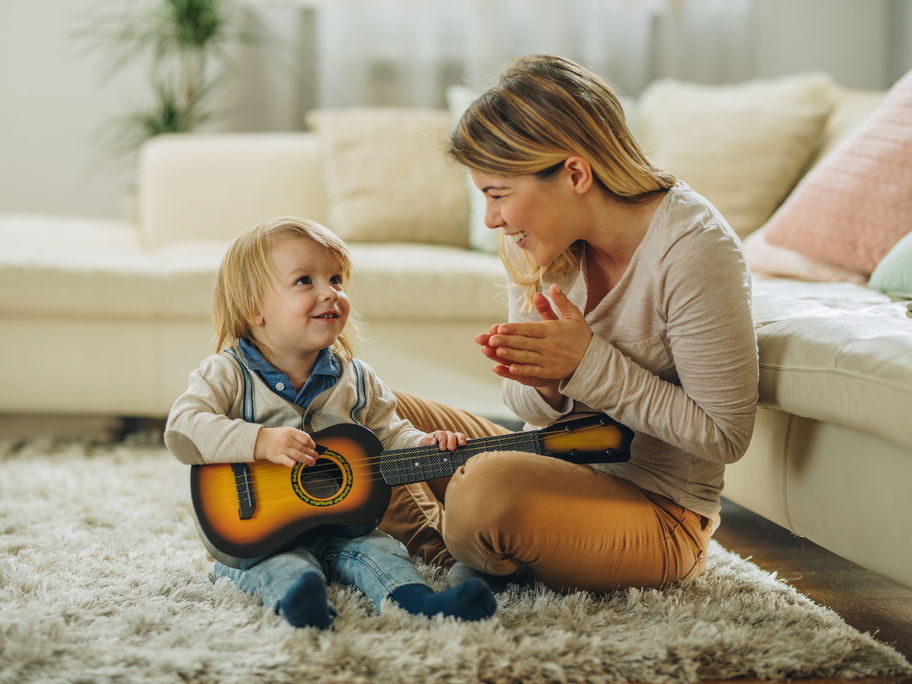 Eine Mama applaudiert ihrem kleinen Sohn, weil er Gitarre spielt