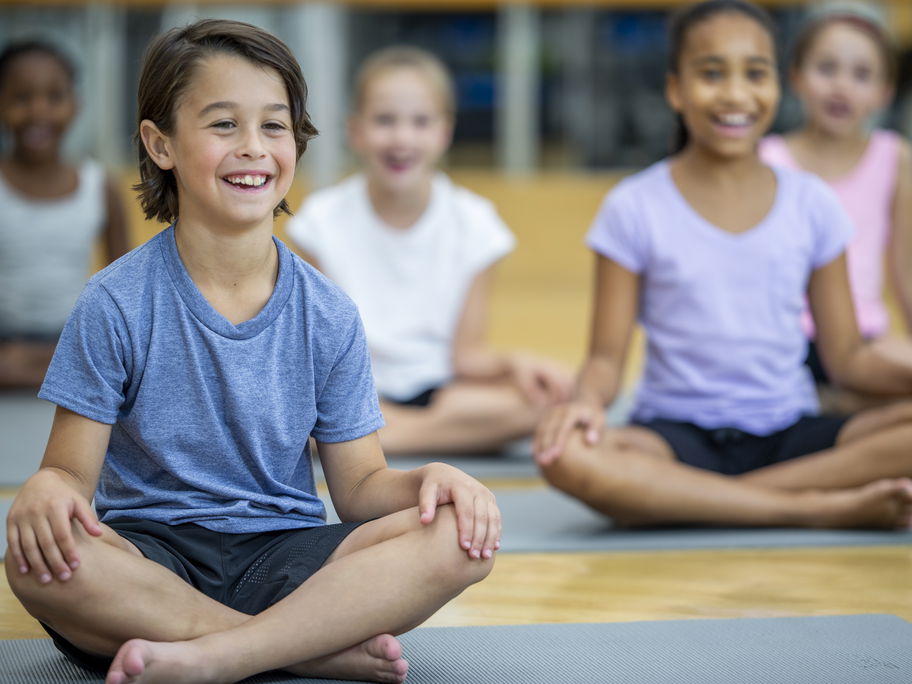Fröhliche Kinder sitzen in der Schule auf Yogamatten.