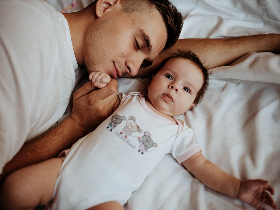 Papa hält beim Schlafen die Hand seines Babys.