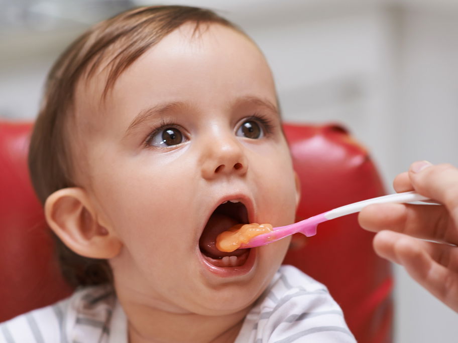 Ein kleines Kind isst einen Löffel Brei aus einem Babygläschen.