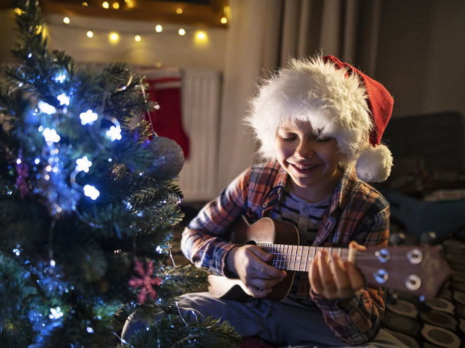 Junge spielt Gitarre und singt ein Weihnachtslied für Kinder unterm Tannenbaum.