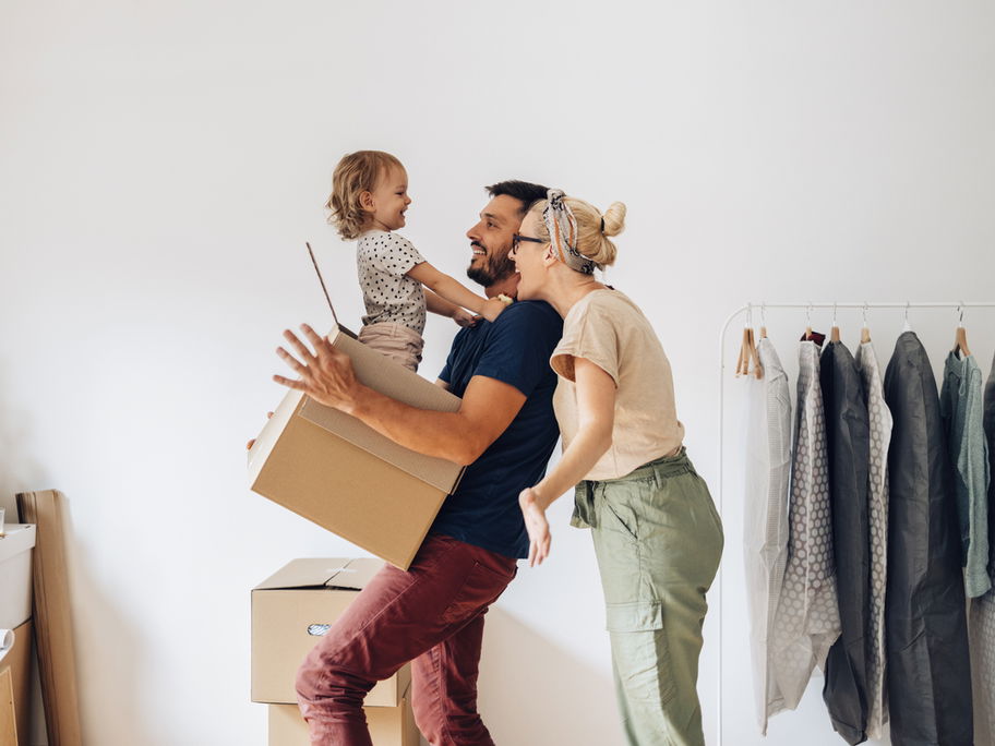 Fröhliche Familie zieht in ein neues Zuhause und das Kleinkind sitzt im Umzugskarton.