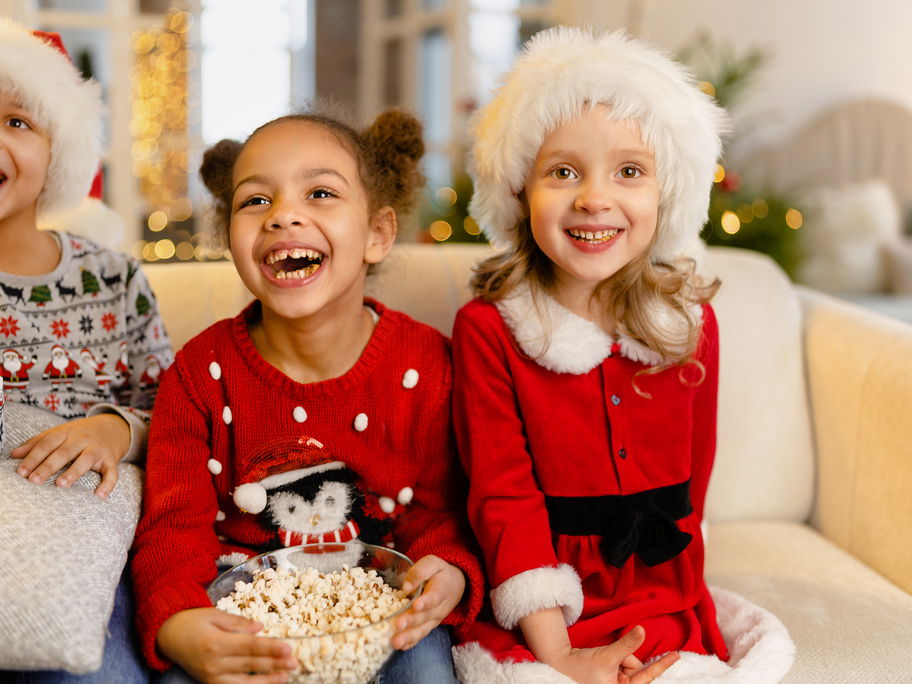Drei weihnachtliche gekleidete Mädchen vor dem Fernseher.