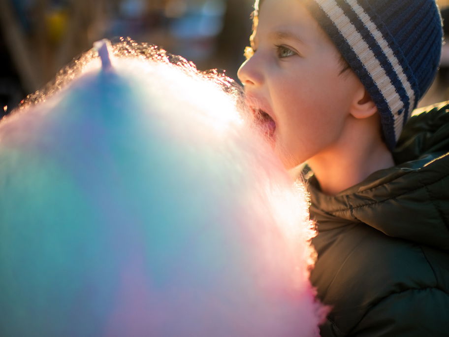 Kleiner Junge isst Zuckerwatte auf dem Weihnachtsmarkt.