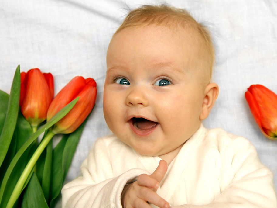 Süßes Baby inmitten von Tulpen zeigt den Daumen hoch