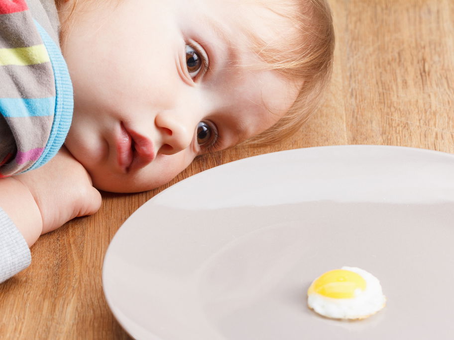 Baby schaut sich ein Spiegelei genau an.