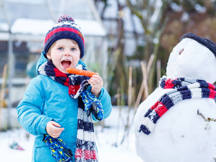 Kind beißt in die Möhre des Schneemanns.