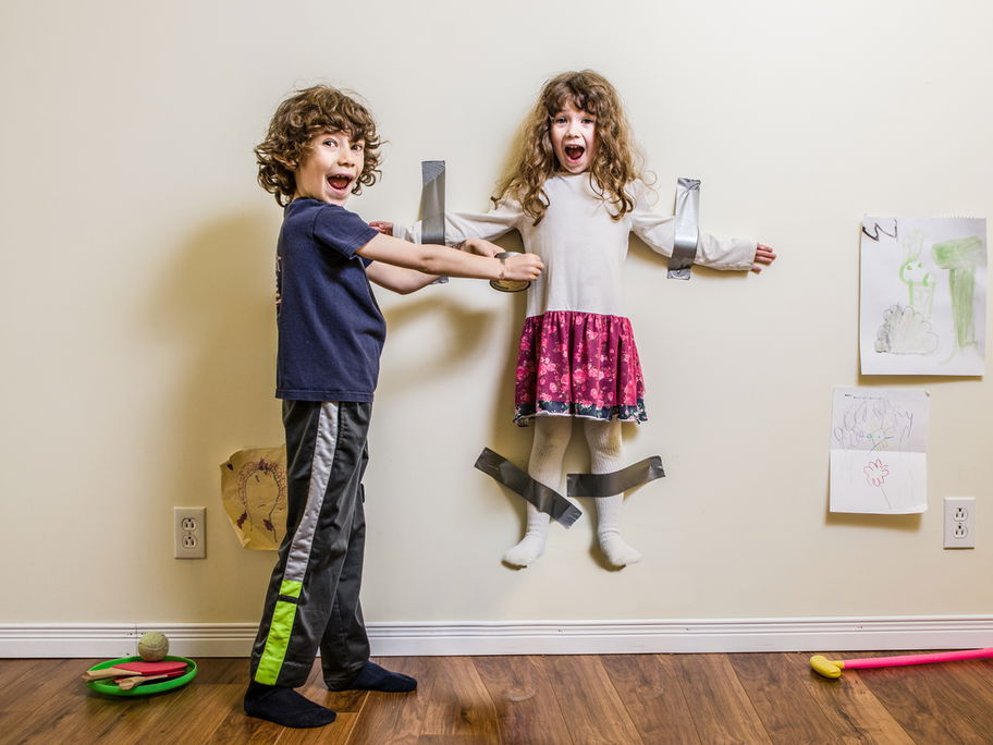 Junge klebt seine kleine Schwester im Spiel an der Wand fest.