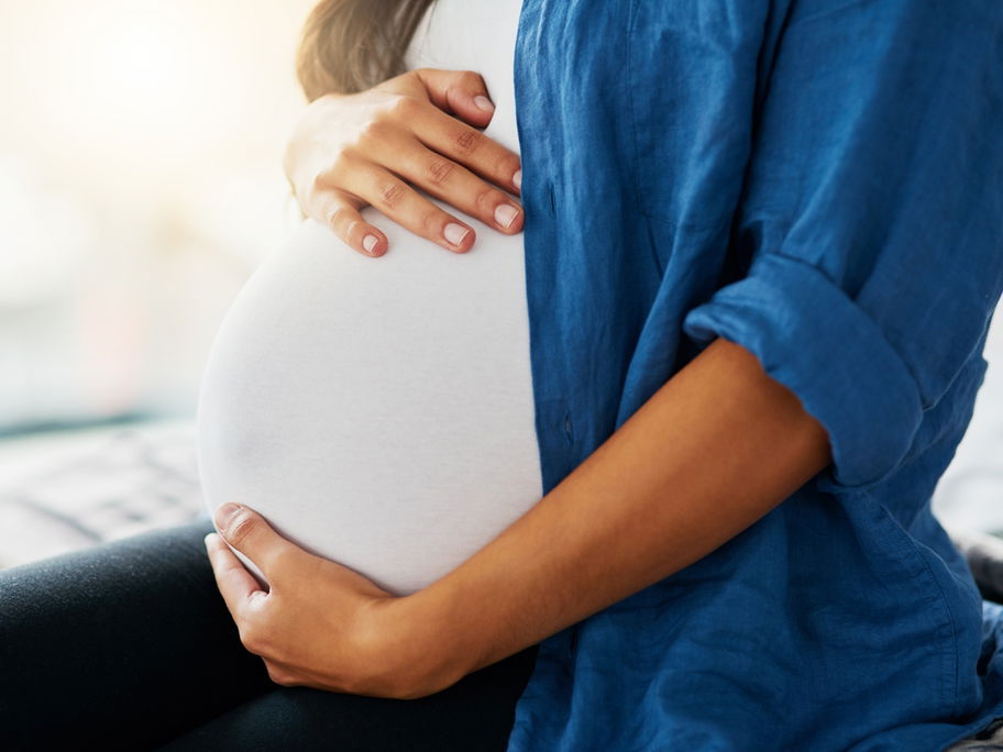 Schwangere Frau hält ihren Babybauch in den Händen.