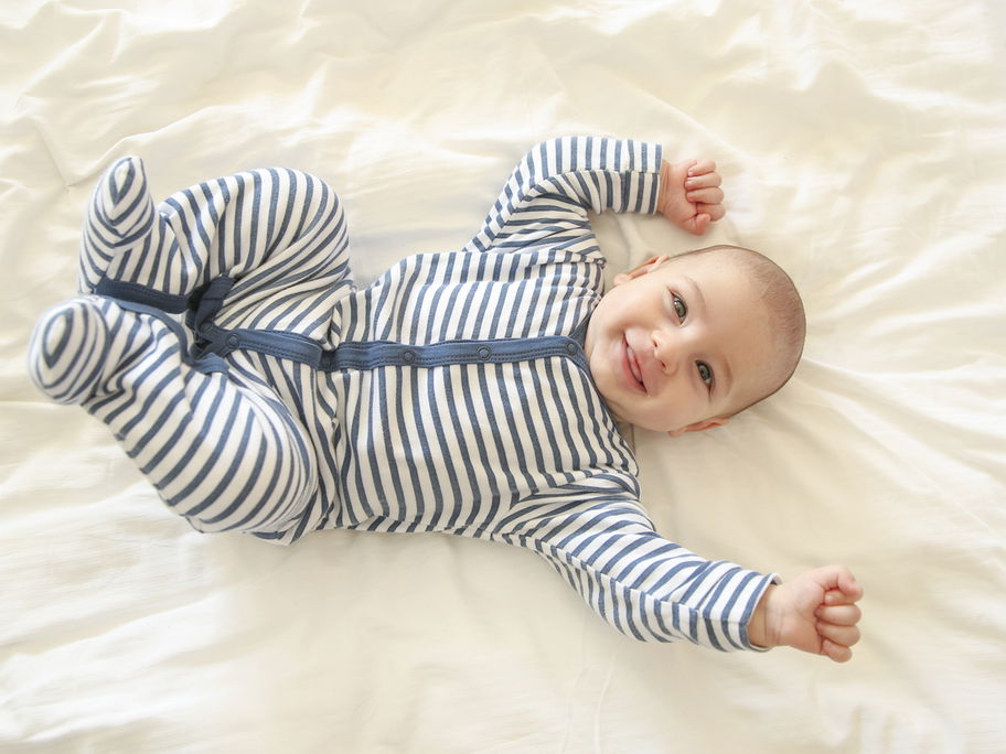 Baby-Junge in einem Strampler hat gute Laune und lacht.