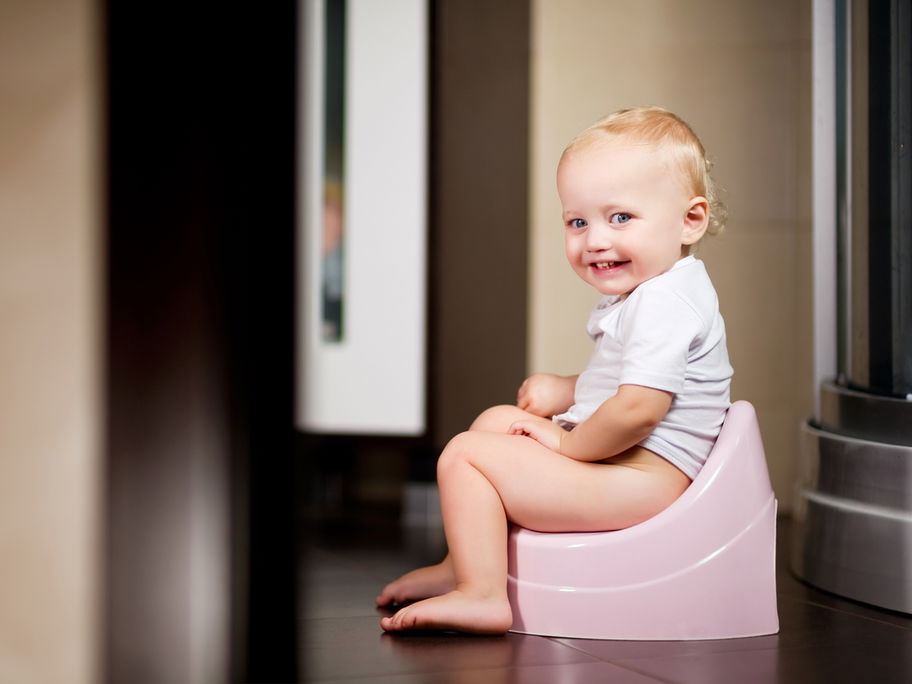 Kleines Mädchen sitzt auf einem Topf im Badezimmer und lächelt.