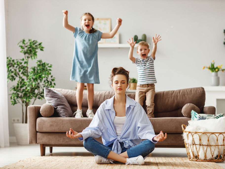 Kinder springen auf dem Sofa, Mutter meditiert.