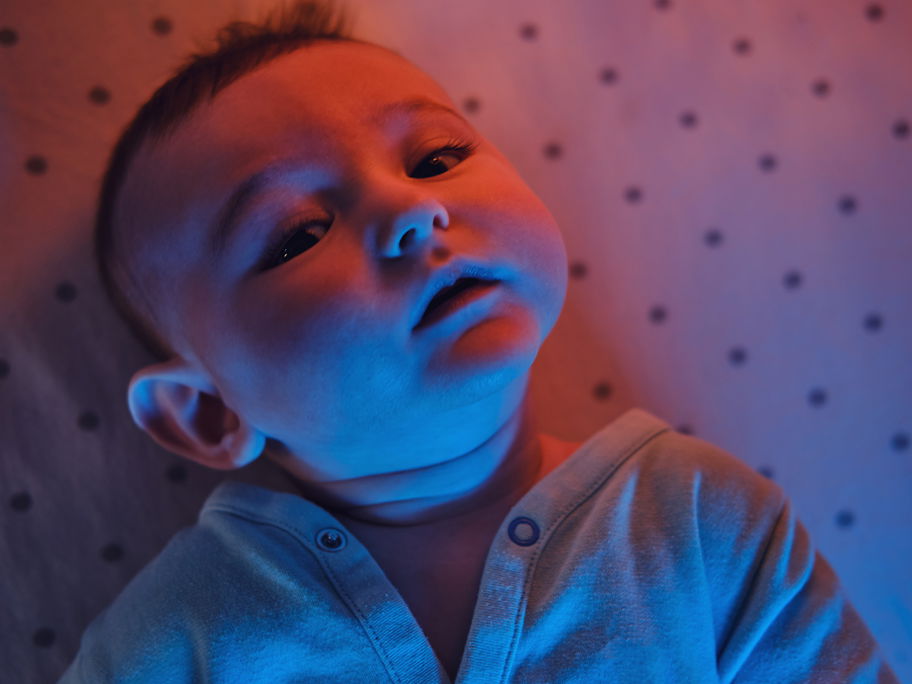 Baby-Junge liegt im Bettchen, im Licht einer Rotlichtlampe.