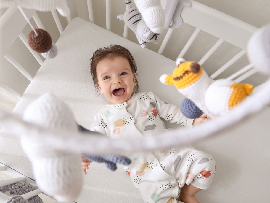Baby liegt im Bett und lacht das über ihm hängende Mobile an.