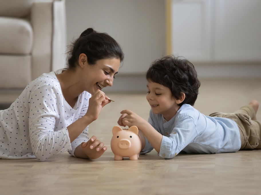 Mutter steckt mit kleinem Jungen Geld ins Sparschwein.