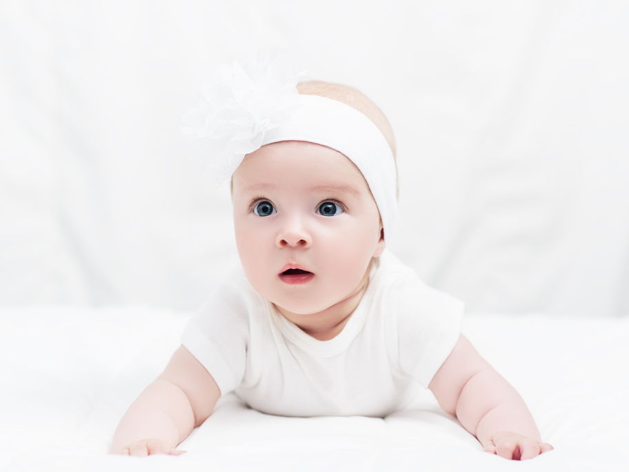 Baby in Bauchlage mit niedlichem Kopfband.