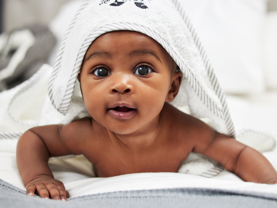 Niedliches, afrikanisches Baby unterm Kapuzenhandtuch.