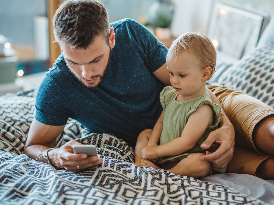 Vater sitzt neben seiner Tochter und guckt aufs Handy