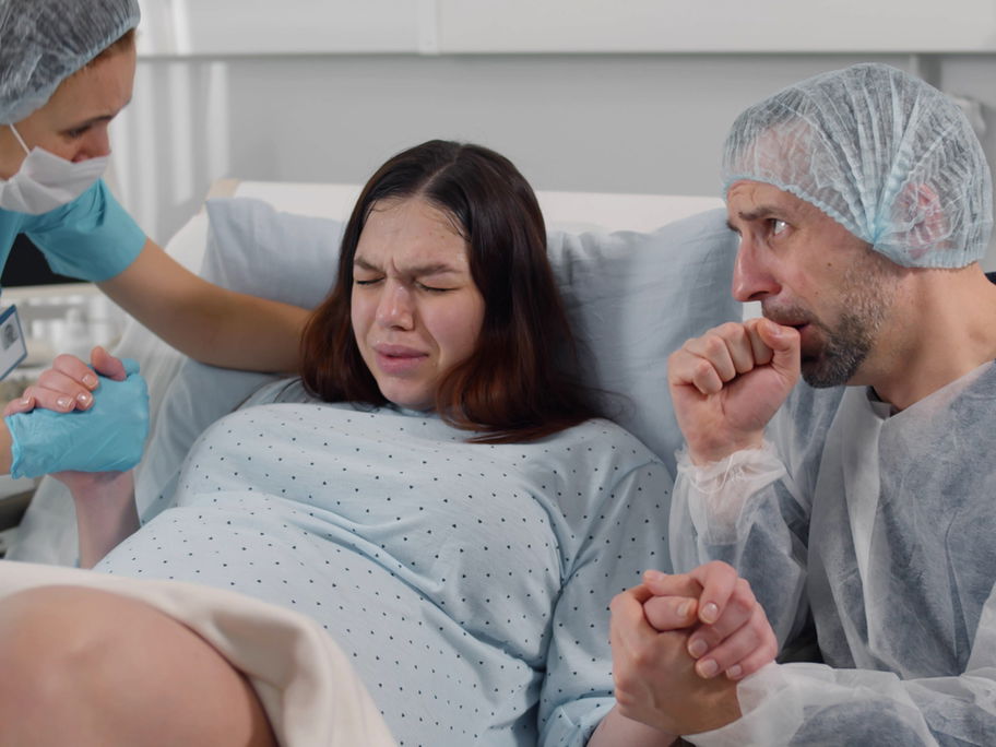 Verängstigter Ehemann, der im Kreißsaal die Hand einer Frau hält