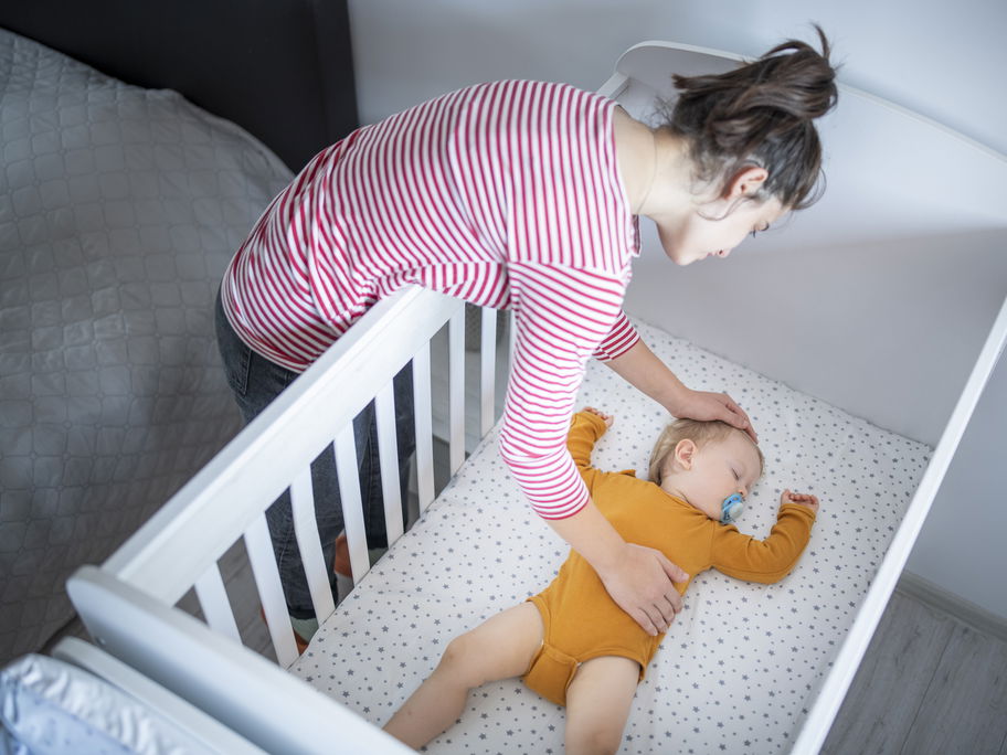 Mutter legt ihr schlafendes Baby ins Bett.