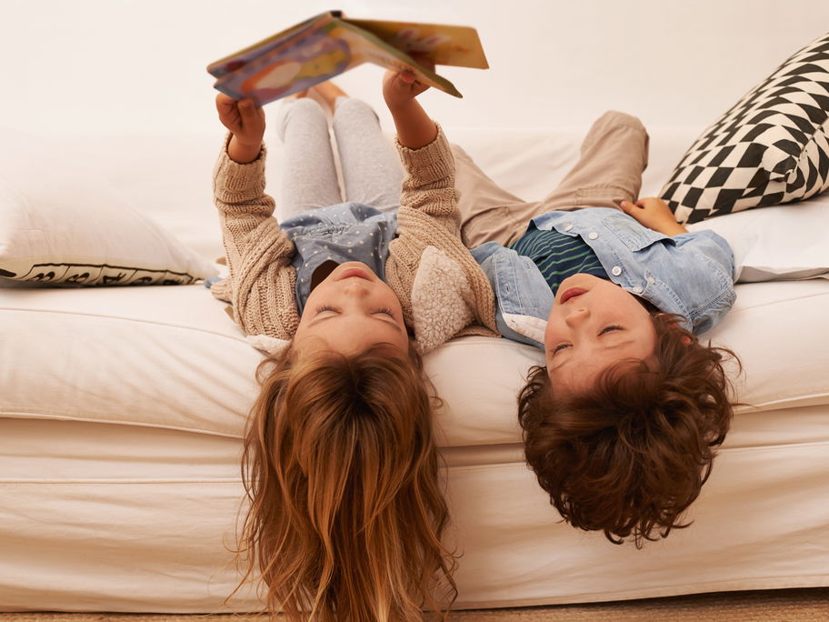Zwei Kinder liegen auf dem Sofa und lesen.