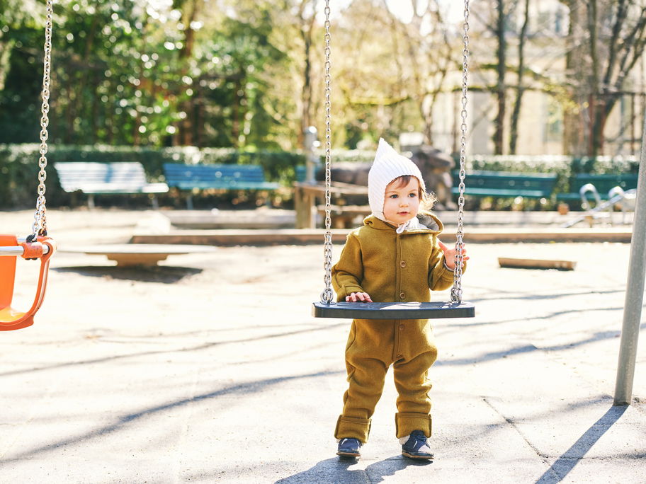 Ein Kleinkind im Wollwalkoverall auf dem Spielplatz