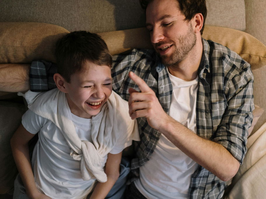 Ein Vater tickt seinen Sohn mit dem Finger an, der bereits zu lachen anfängt.